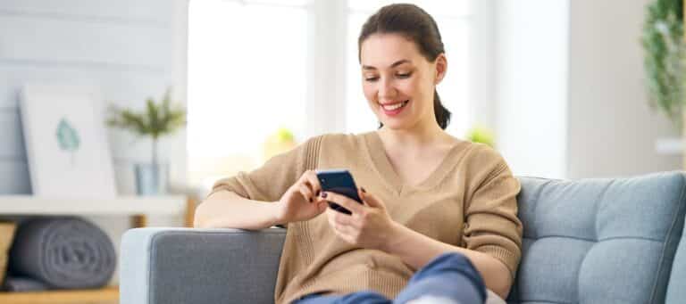 Smiling woman sitting on a couch using her smartphone at home