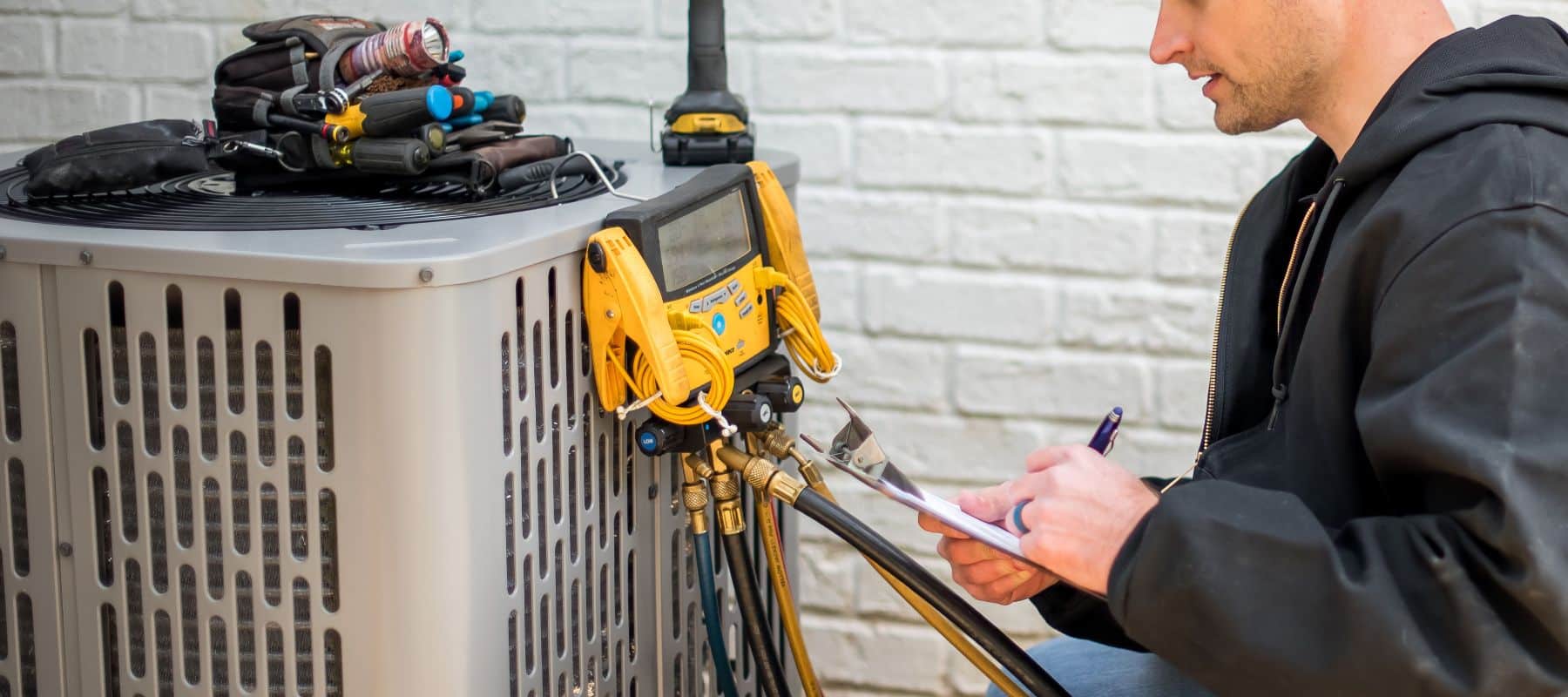 technician performing heater maintenance with a digital manifold pressure checker on outdoor hvac unit