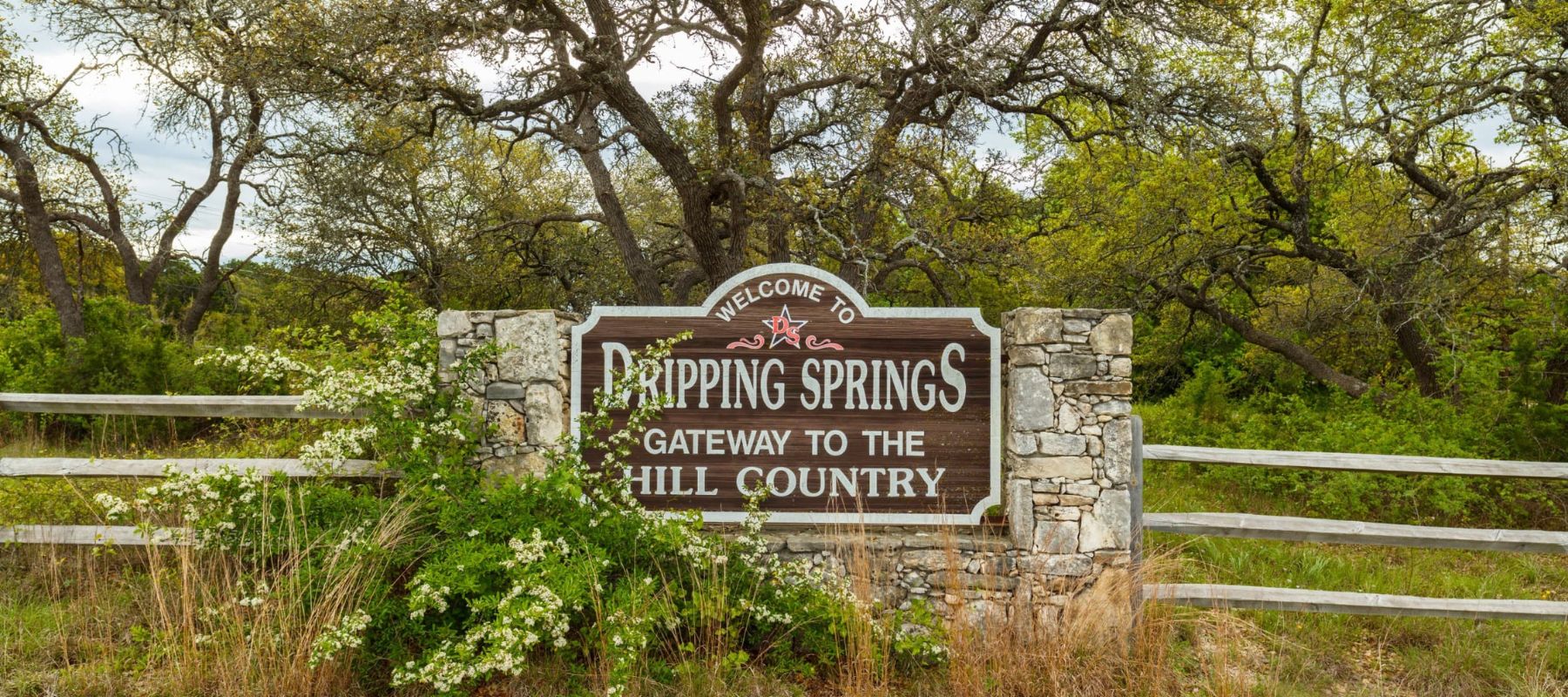 welcome to dripping springs gateway to the hill country sign positioned outside surrounded by trees