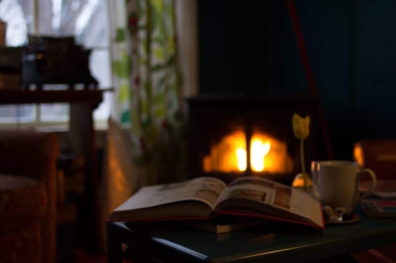 peaceful dark room with fire blazing in a small chimney in the background, open book and cup of coffee in the foreground