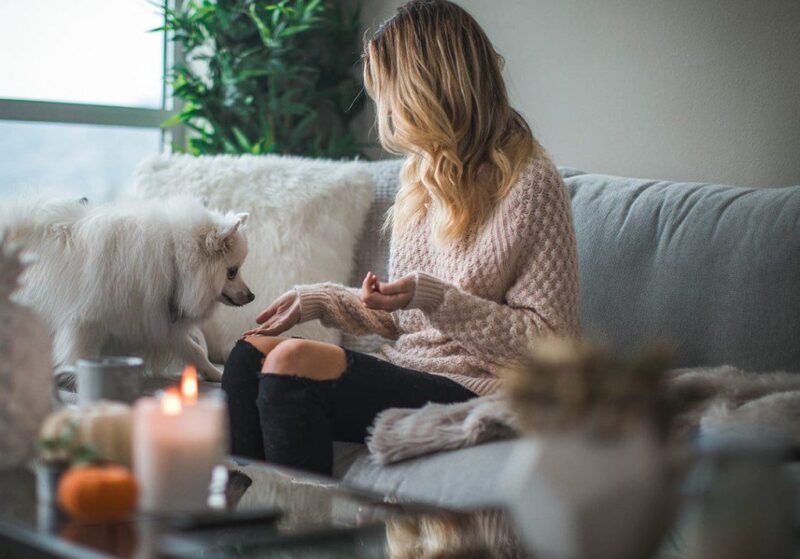 homeowner in her living room sitting on her couch reaching her hand out to let her small white fluffy dog to sniff it
