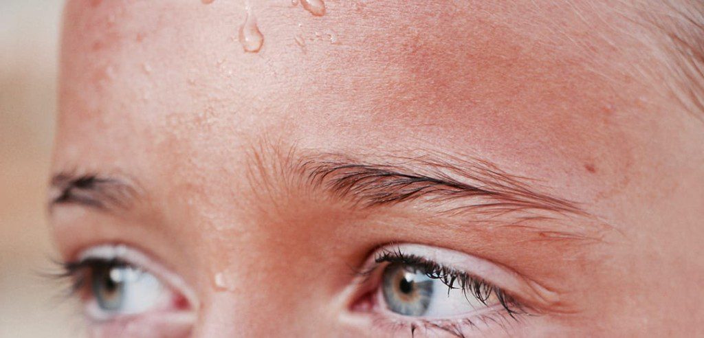 closeup of young person eyes and eyebrows with a bead of sweat going down their forehead