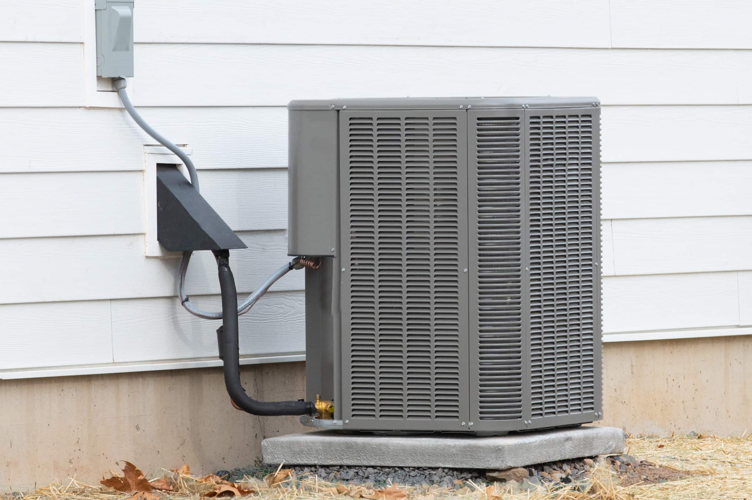 A gray outdoor HVAC unit on a concrete slab next to a white siding wall.
