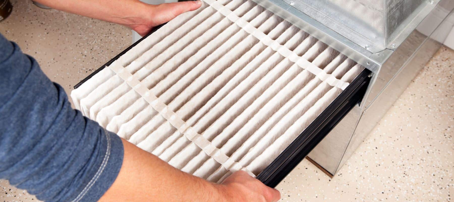 Person sliding a clean air filter into a home HVAC system